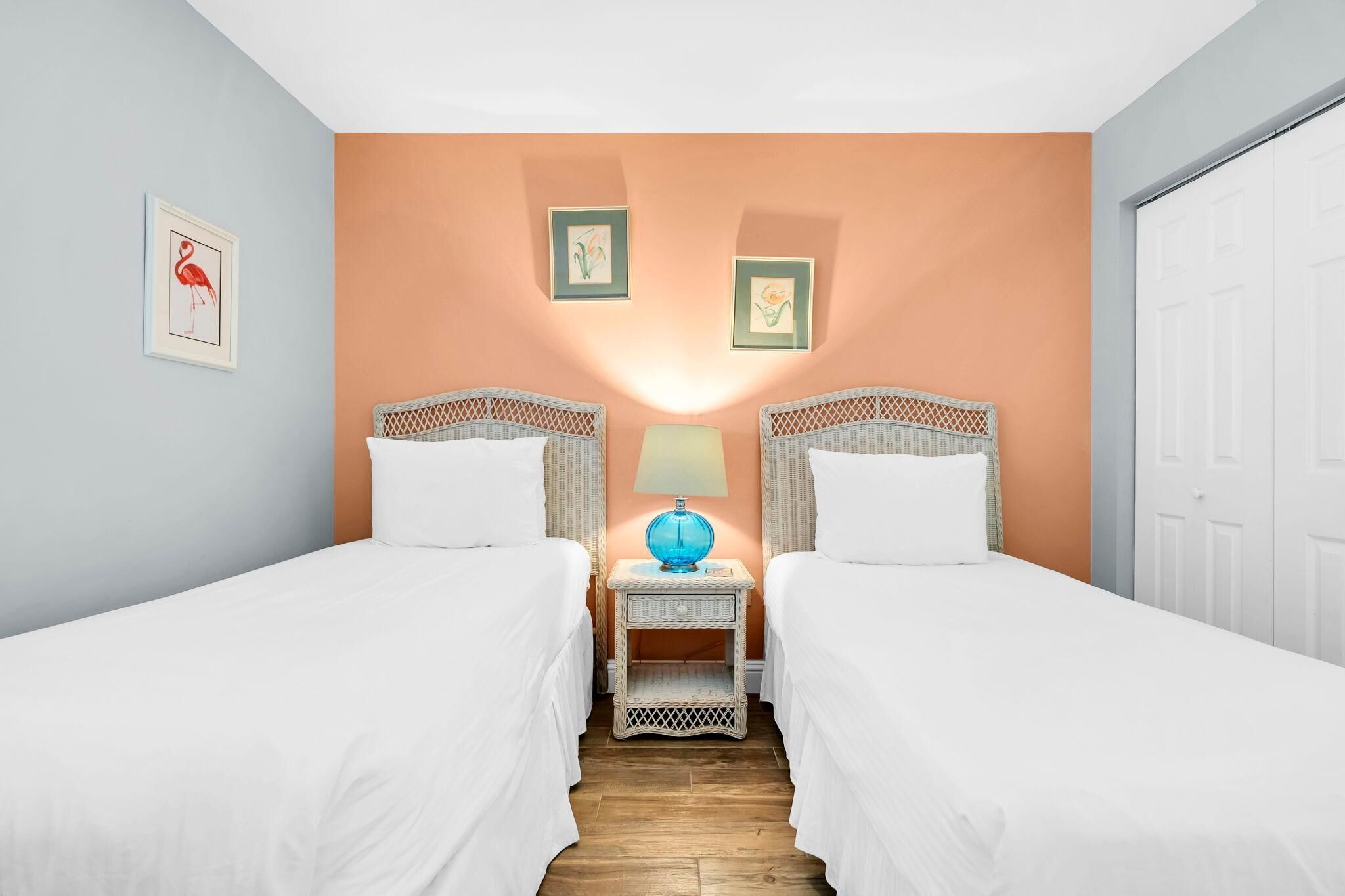 A hotel room with two single beds, a nightstand with a lamp, and wall art.