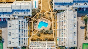 Vue aérienne d’un hôtel composé de plusieurs bâtiments, avec une piscine centrale et de nombreux espaces verts environnants.