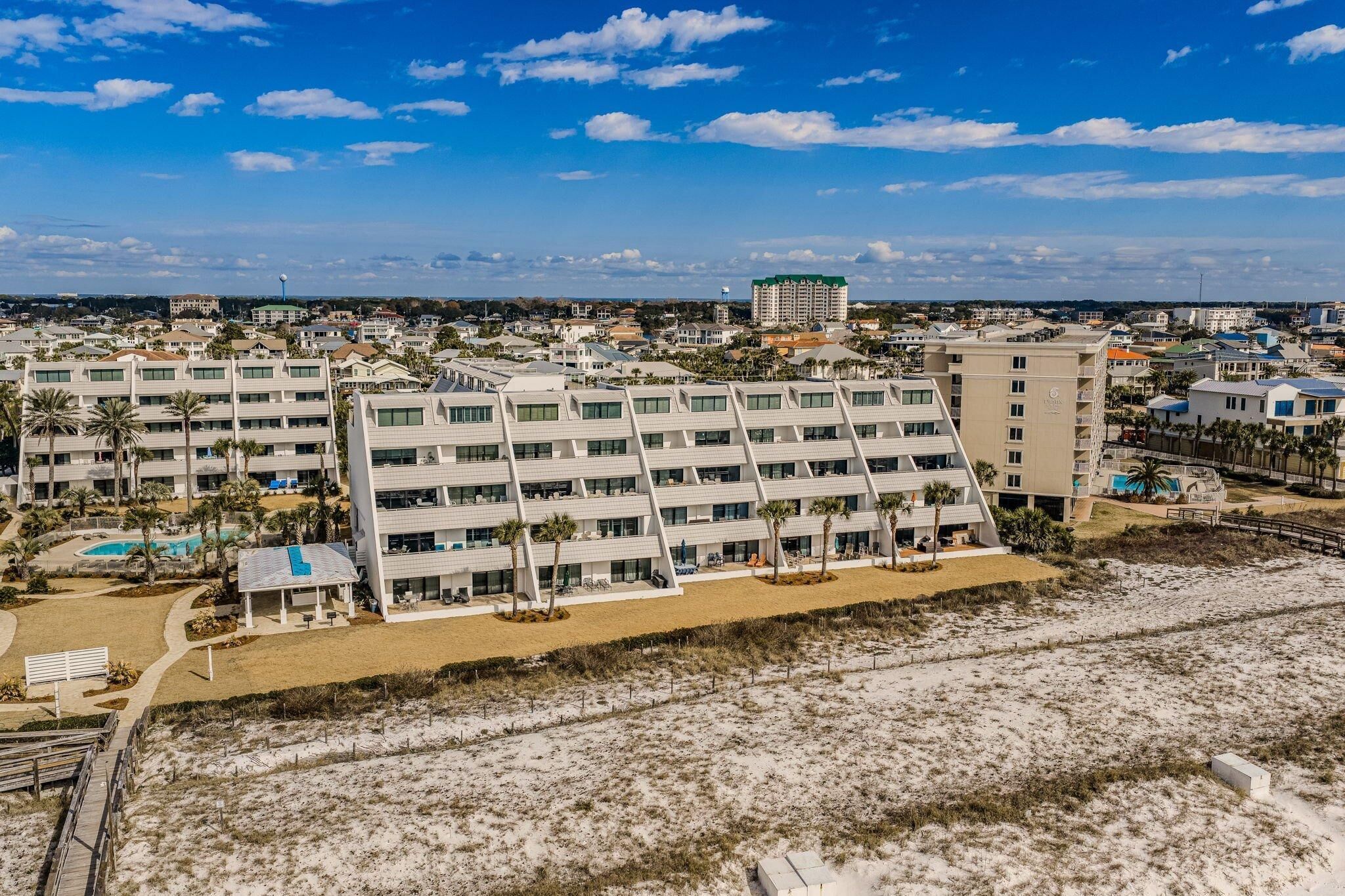A modern hotel with multiple floors, a swimming pool, and a beach area.