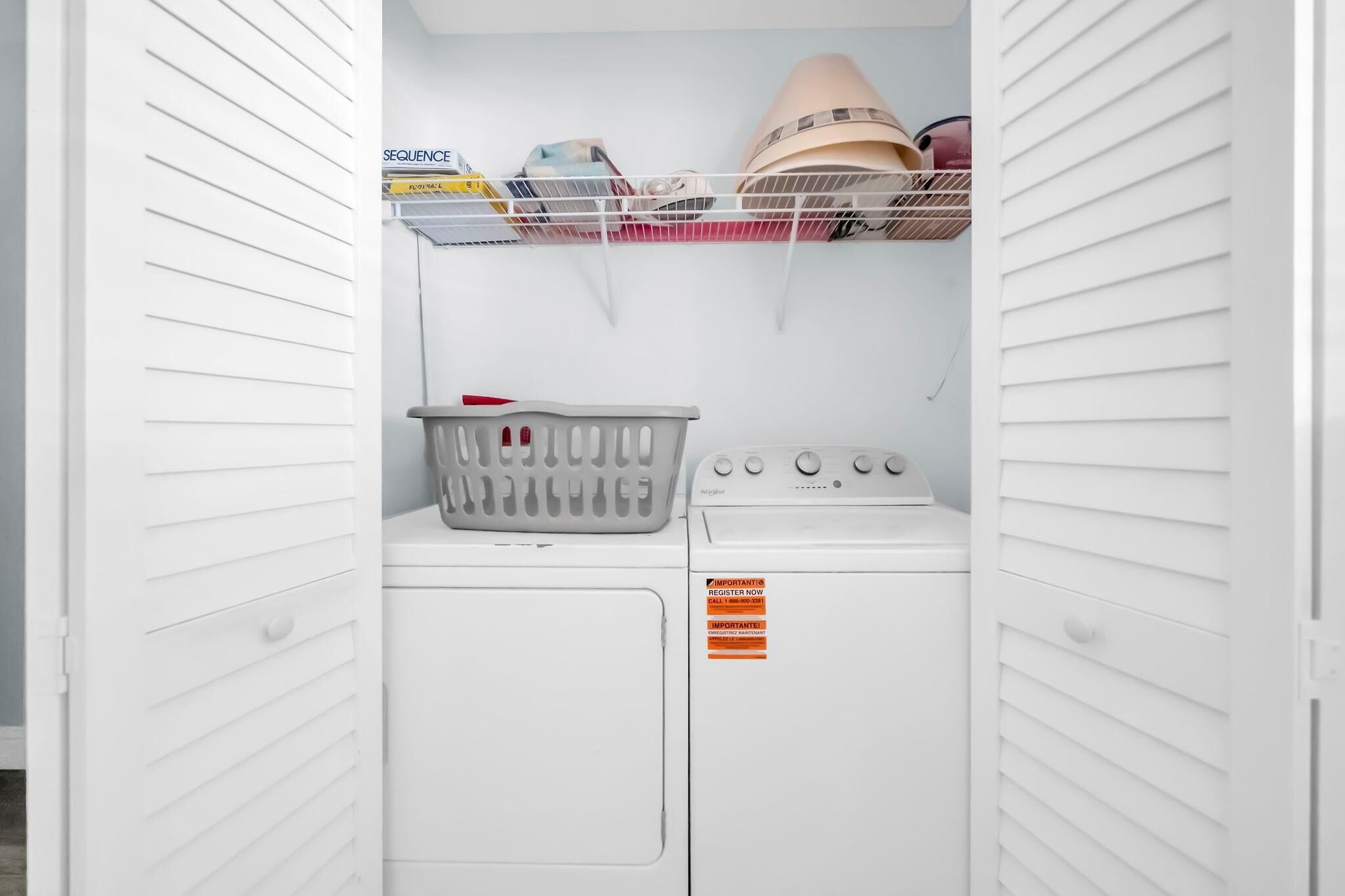 A laundry room with a washing machine, a dryer, and a shelf with hats and other items.