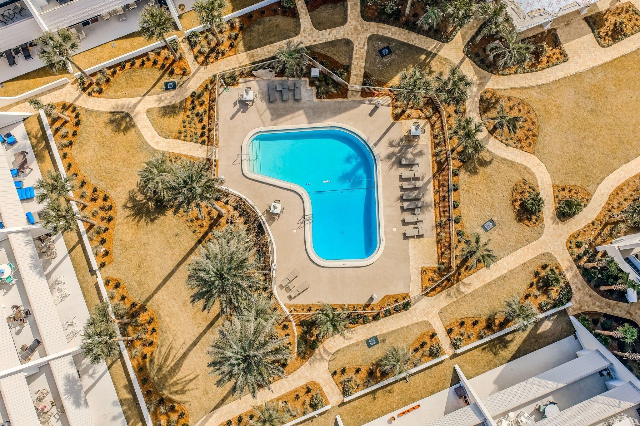 Oversigtsbillede af et resort med en central swimmingpool, palmer og liggestole.