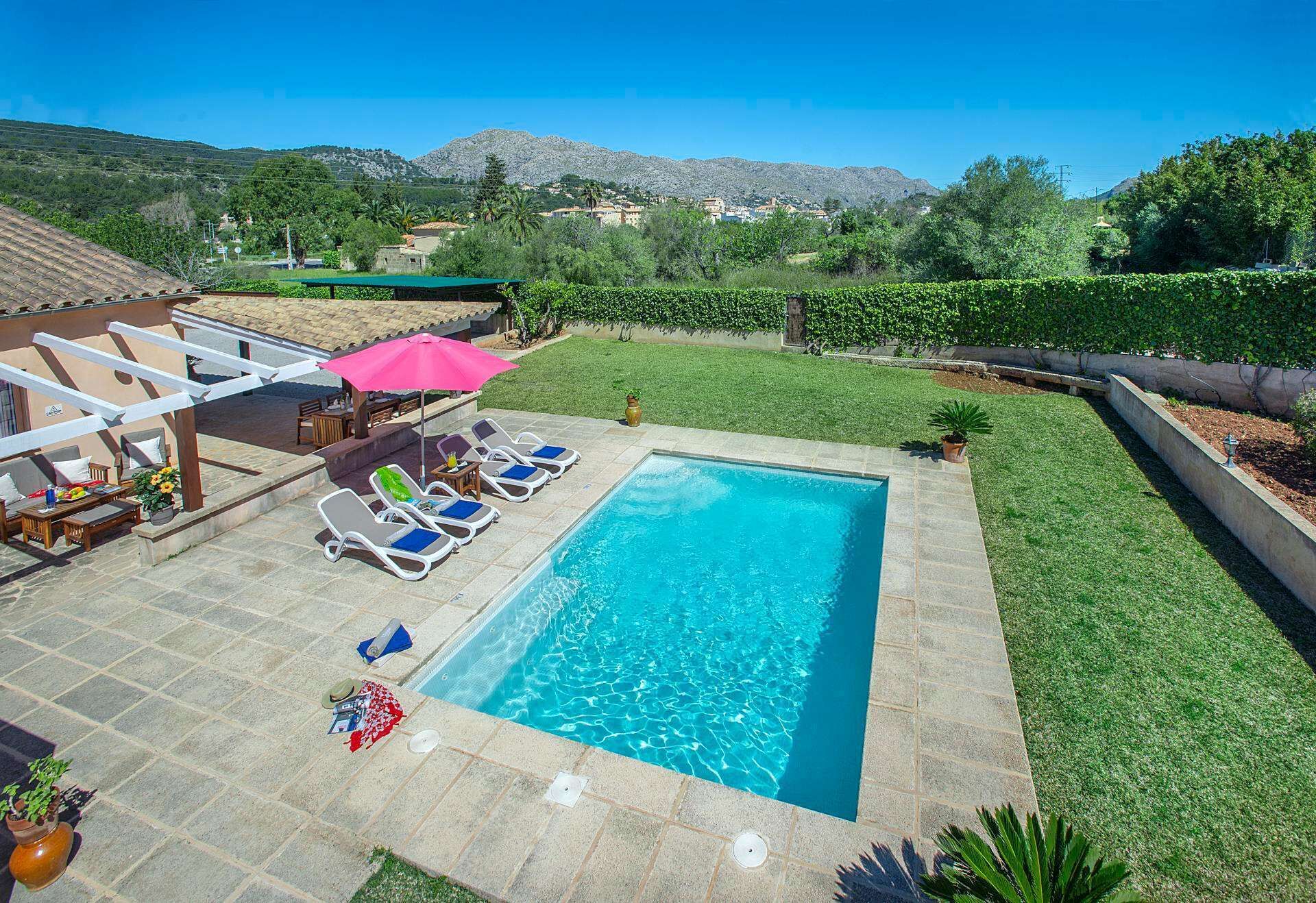 A rectangular swimming pool with lounge chairs and a table, surrounded by a well-maintained lawn and a view of mountains in the background.