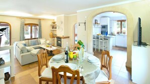 A spacious living area with a dining table set for four, a sofa, and a kitchen visible through an archway. - Pretty Stone Finca, A/C, Private Pool, Large Grounds & Rural Views just 5mins from Old Town Pollenca (Pollença)