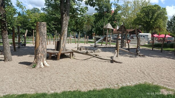 Un parque infantil con estructuras de madera, un tobogán y una zona cubierta.