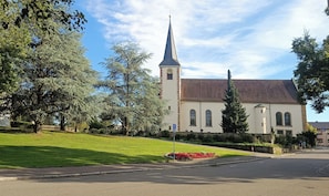 En kirke med et højt spir og et klokketårn, omgivet af træer og en græsplæne.