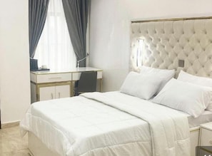 A hotel room with a bed, a desk, and a chair. - De Grand Hotel and Rooftop (Calabar)
