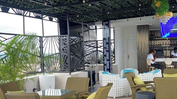 An indoor seating area with wicker furniture and a bar in the background. - De Grand Hotel and Rooftop (Calabar)