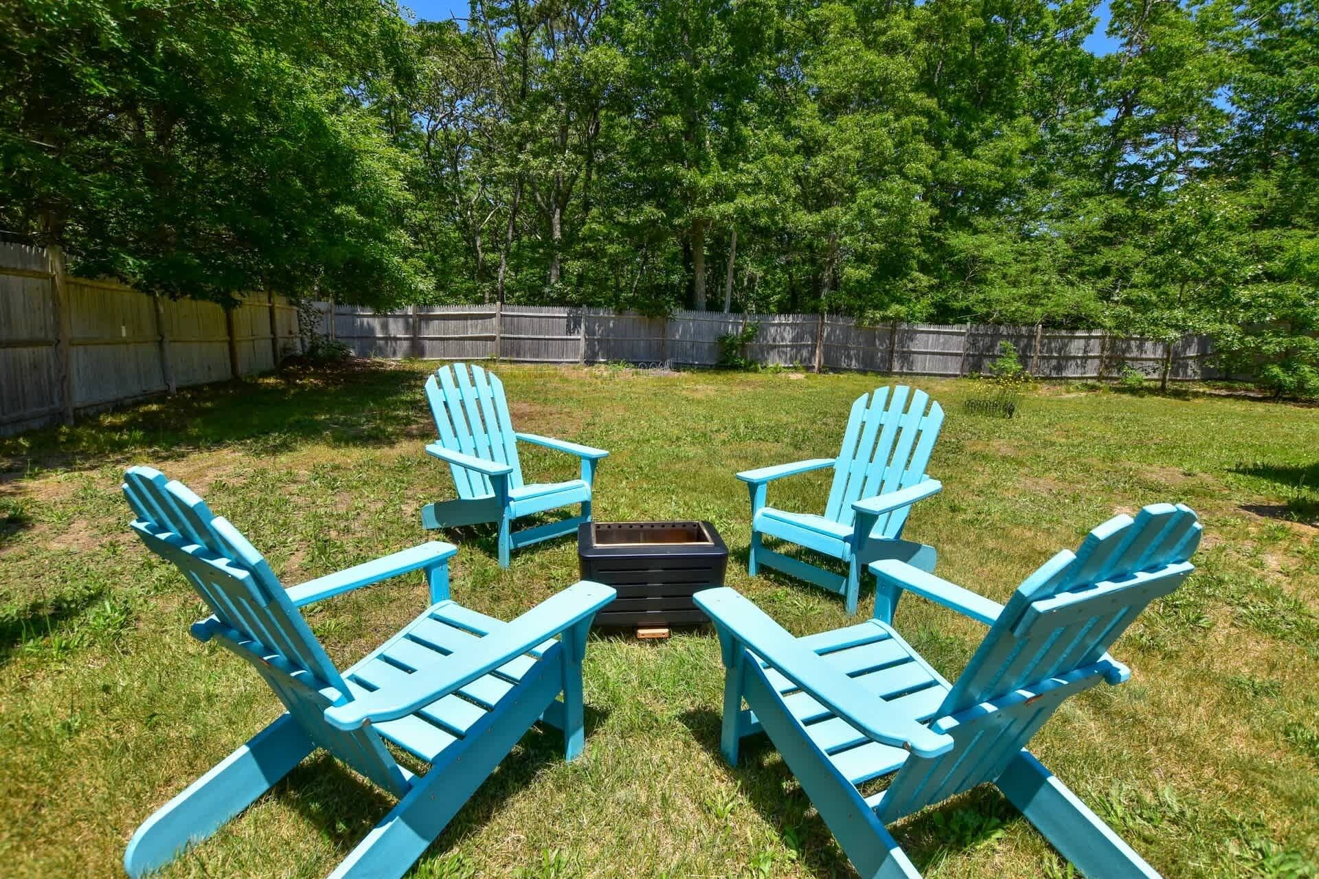 A backyard with four blue Adirondack chairs arranged in a circle around a black table.