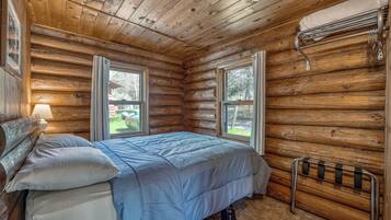 Un dormitorio tipo cabaña de madera con una cama, una mesita de noche, una ventana y un radiador.