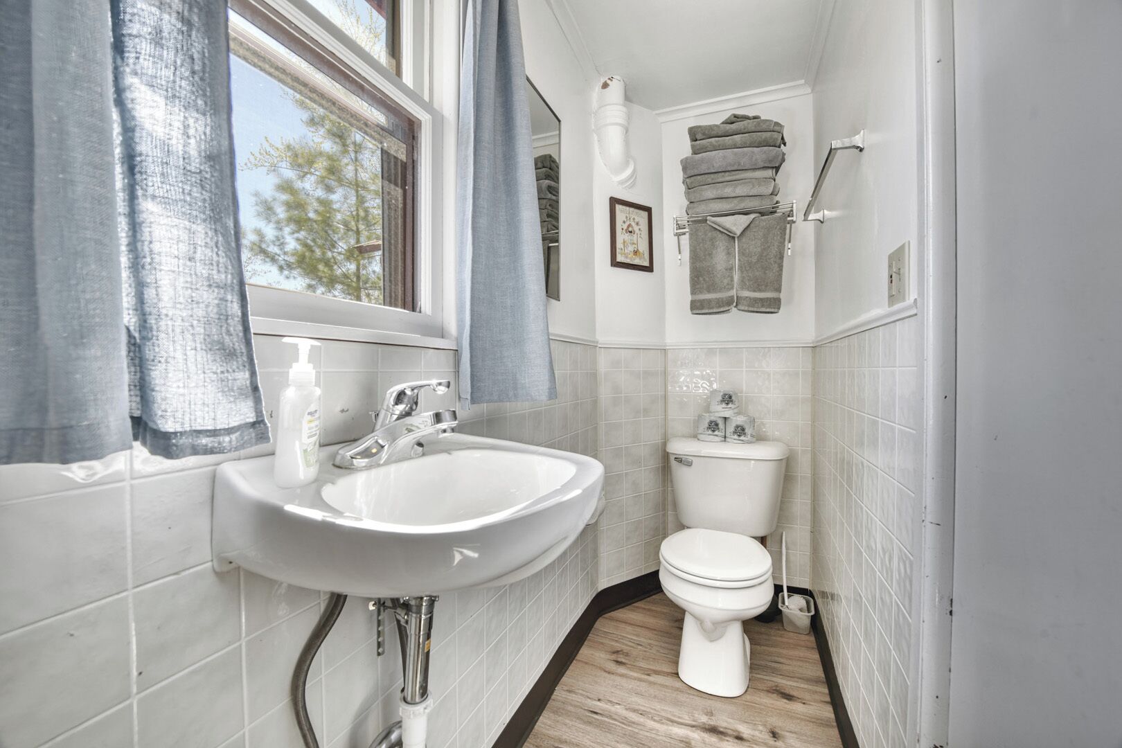 Une petite salle de bain avec un lavabo blanc, des toilettes et une fenêtre avec des rideaux.