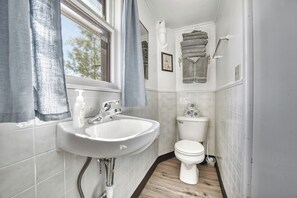 Un bagno piccolo con un lavandino bianco, un WC e una finestra con tende.