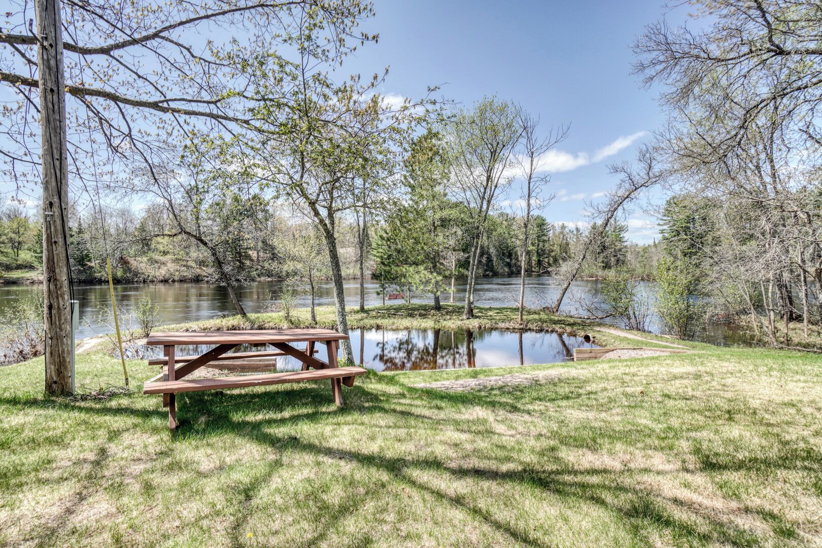 A picnic table by a lake with trees and a clear sky.