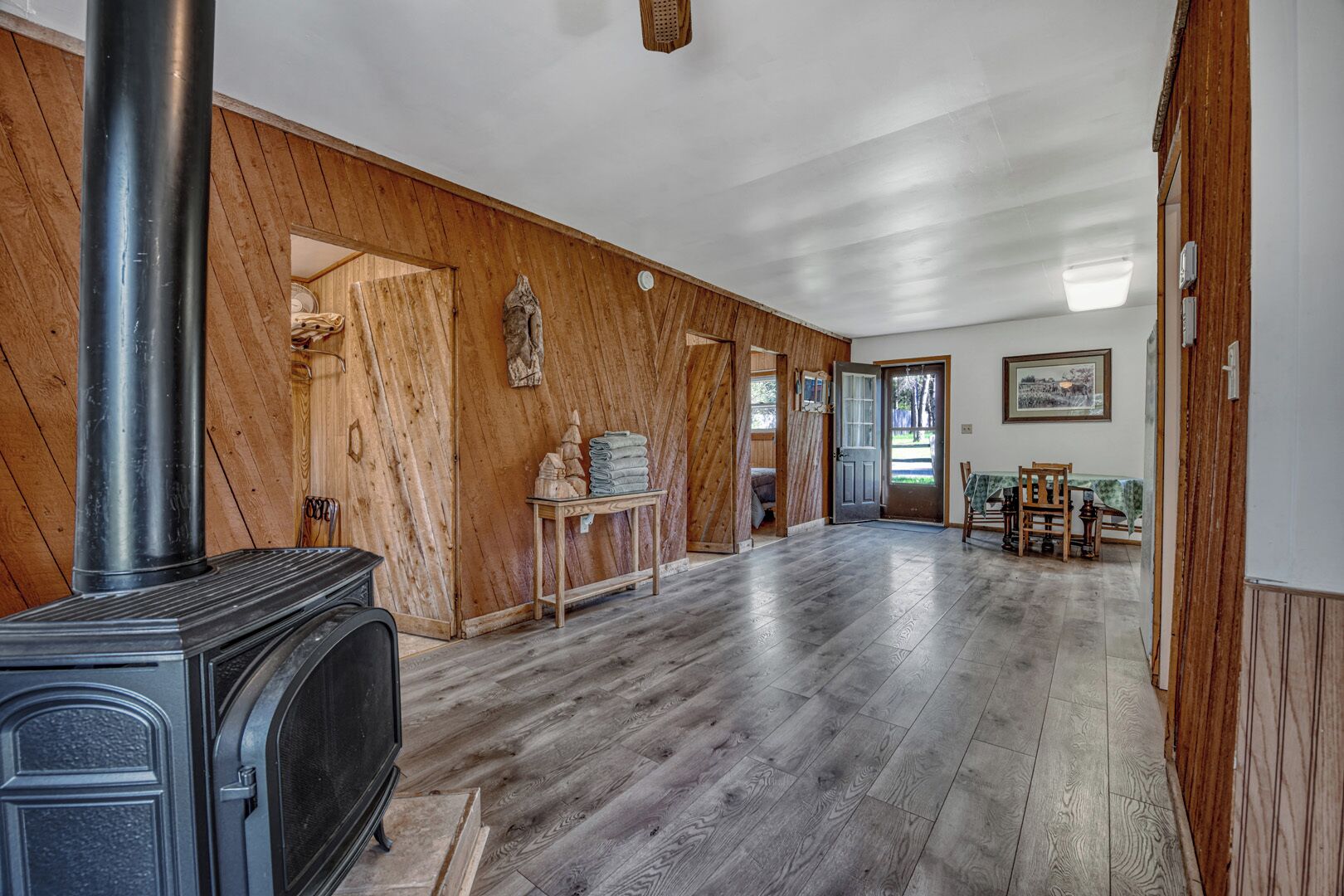 A spacious room with a wood-paneled wall, a fireplace, a dining area with a table and chairs, and a door leading to another room.
