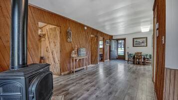 A spacious room with a wood-paneled wall, a fireplace, a dining area with a table and chairs, and a door leading to another room.