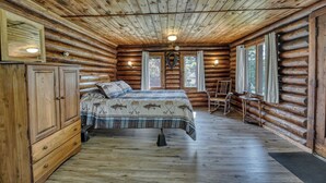 A log cabin bedroom with a bed, wooden wardrobe, and a rocking chair. - Edgewater Resort (Iron Mountain)