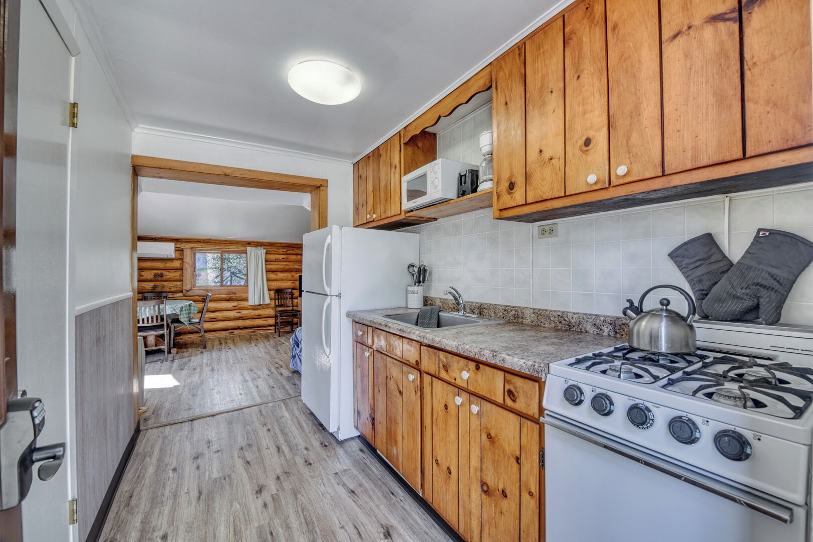 A compact kitchen with wooden cabinets, a white refrigerator, a gas stove, and a microwave.