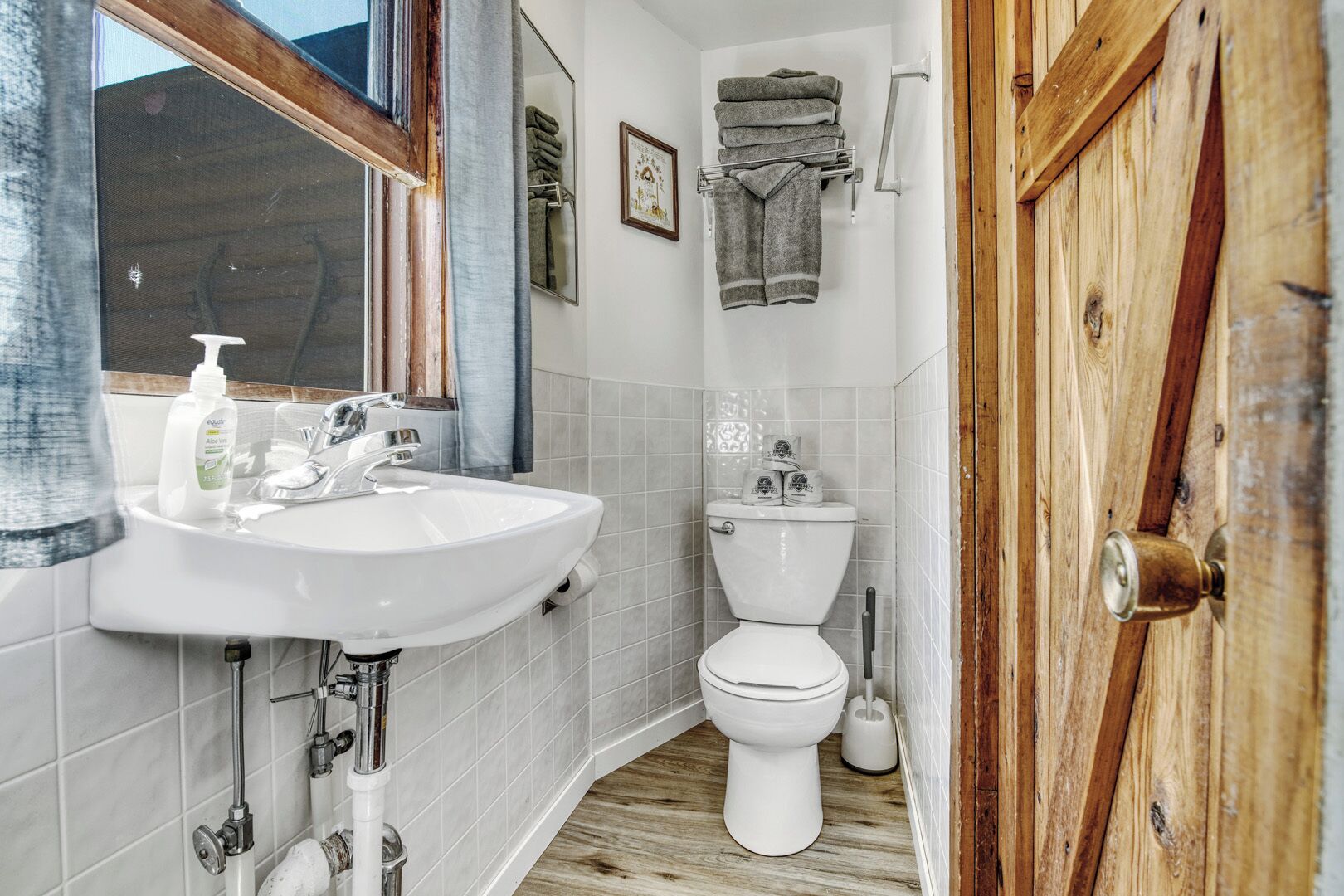 Baño con lavamanos blanco, inodoro y puerta de madera.