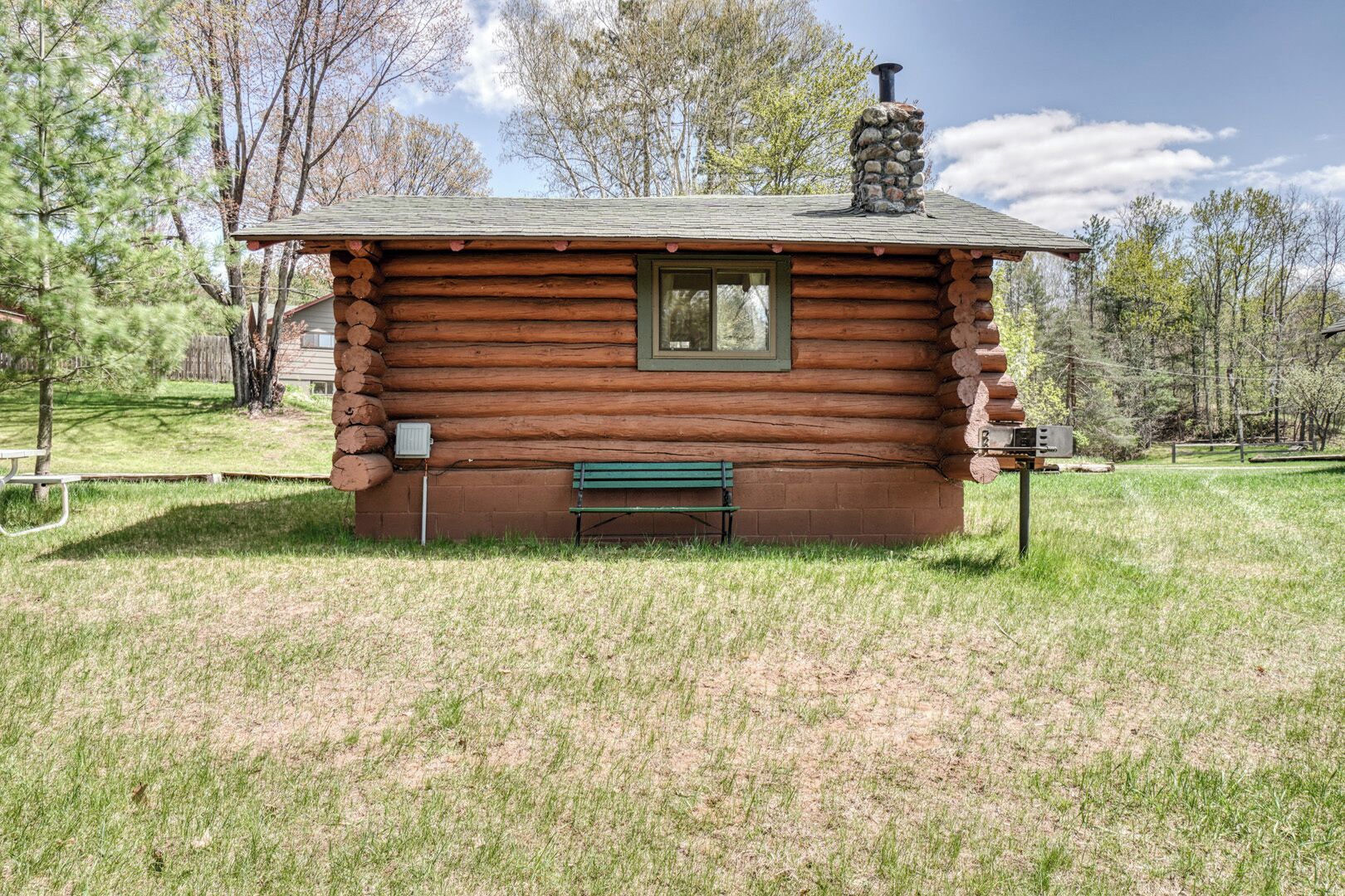 A log cabin with a chimney, a window, and a bench in front.