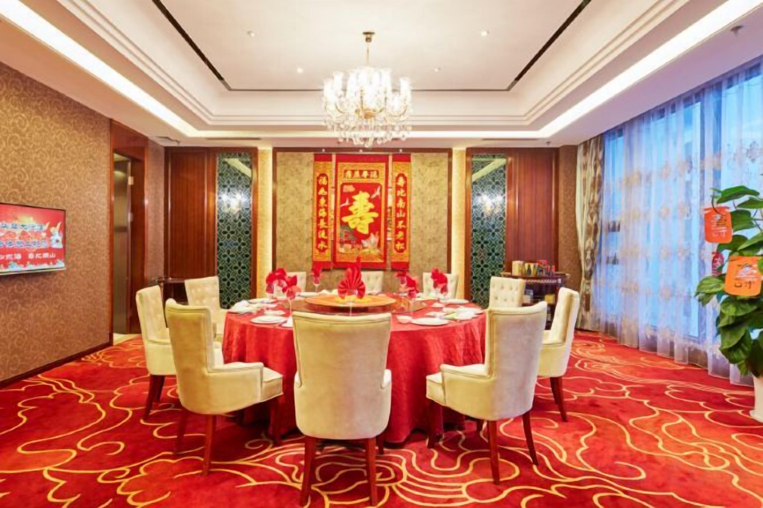 A conference room with round tables, chairs, a chandelier, and a red carpeted floor.