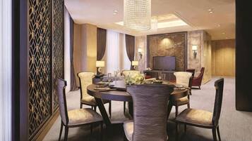 A hotel dining room with a round table, chairs, a chandelier, and a television.