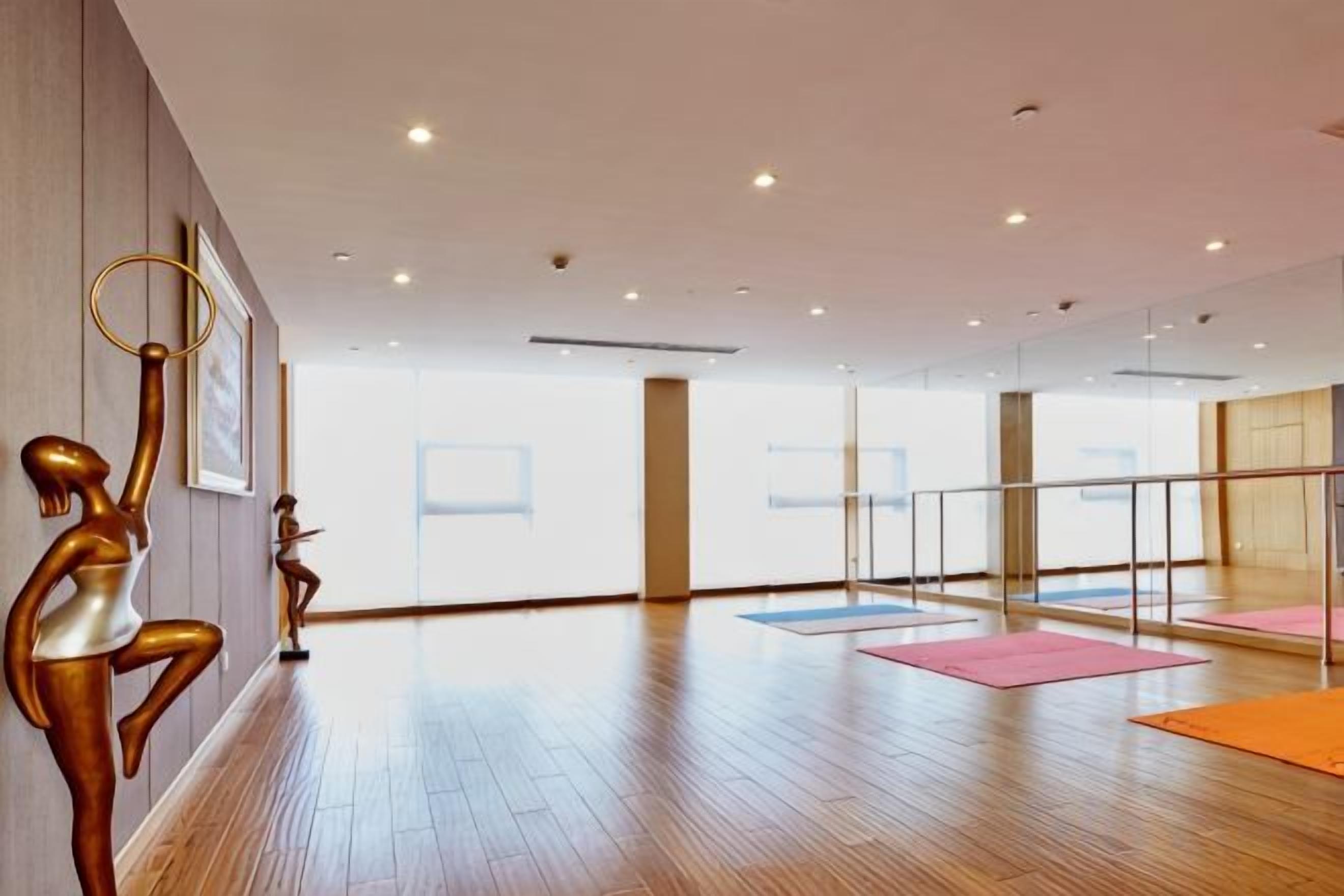 A spacious room with wooden flooring, a glass partition, and exercise mats.