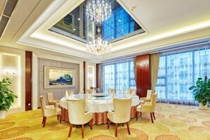 A hotel dining room with a round table, chairs, a chandelier, large windows, and a painting on the wall. - Huaxi Hotel (Laixi)