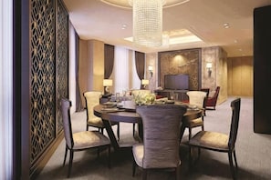 Une salle à manger d’hôtel avec une table ronde, des chaises, un lustre et un téléviseur.