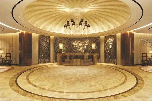 A spacious lobby with a central reception desk, a large chandelier, and a circular marble floor.