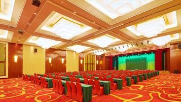 A conference room with rows of chairs, a stage, and a carpeted floor.