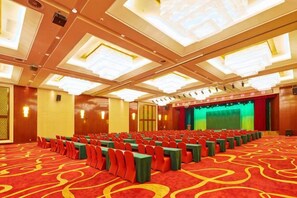 A conference room with rows of chairs, a stage, and a carpeted floor.