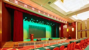 A conference room with a stage, a long table with chairs, and a red carpet.