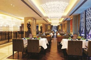 A restaurant with multiple tables, a chandelier, and a view of the city. - Huaxi Hotel (Laixi)