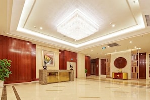 A hotel lobby with a reception desk, a chandelier, and a large plant. - Huaxi Hotel (Laixi)