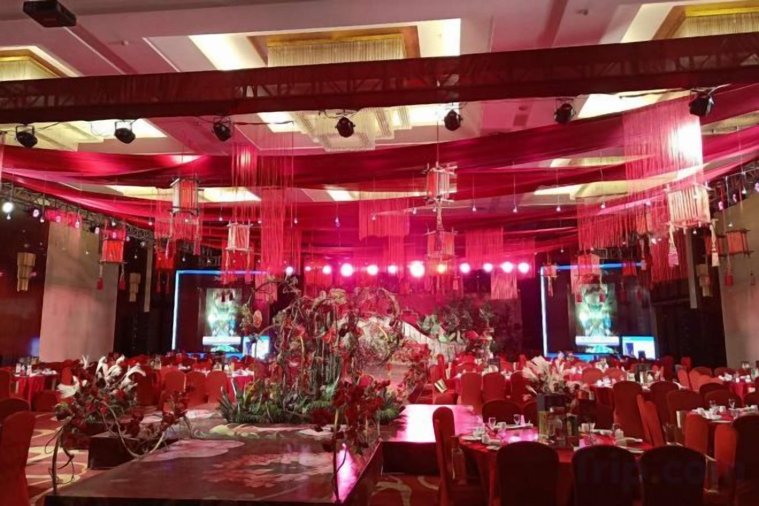 A banquet hall with tables set for a formal event, red drapery, and a stage with lighting.