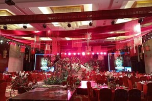 A banquet hall with tables set for a formal event, red drapery, and a stage with lighting. - Huaxi Hotel (Laixi)
