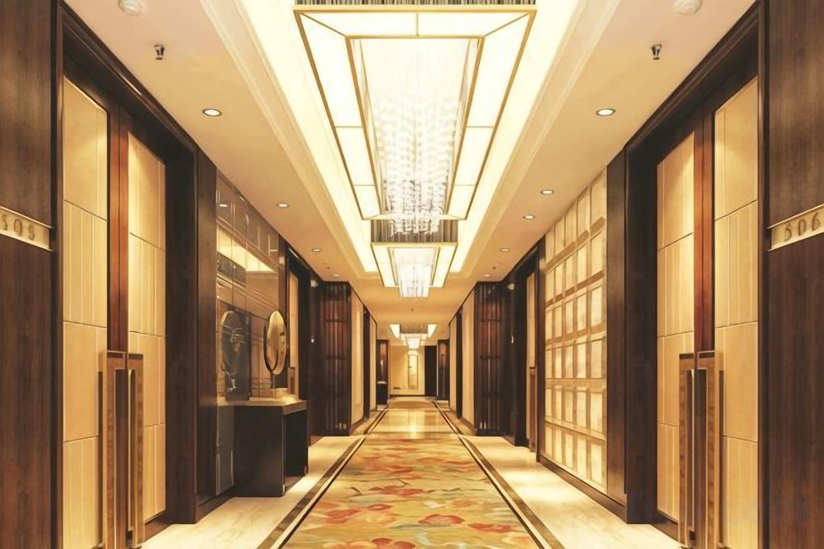 A long, narrow hallway with a patterned carpet, wooden walls, and a central light fixture.