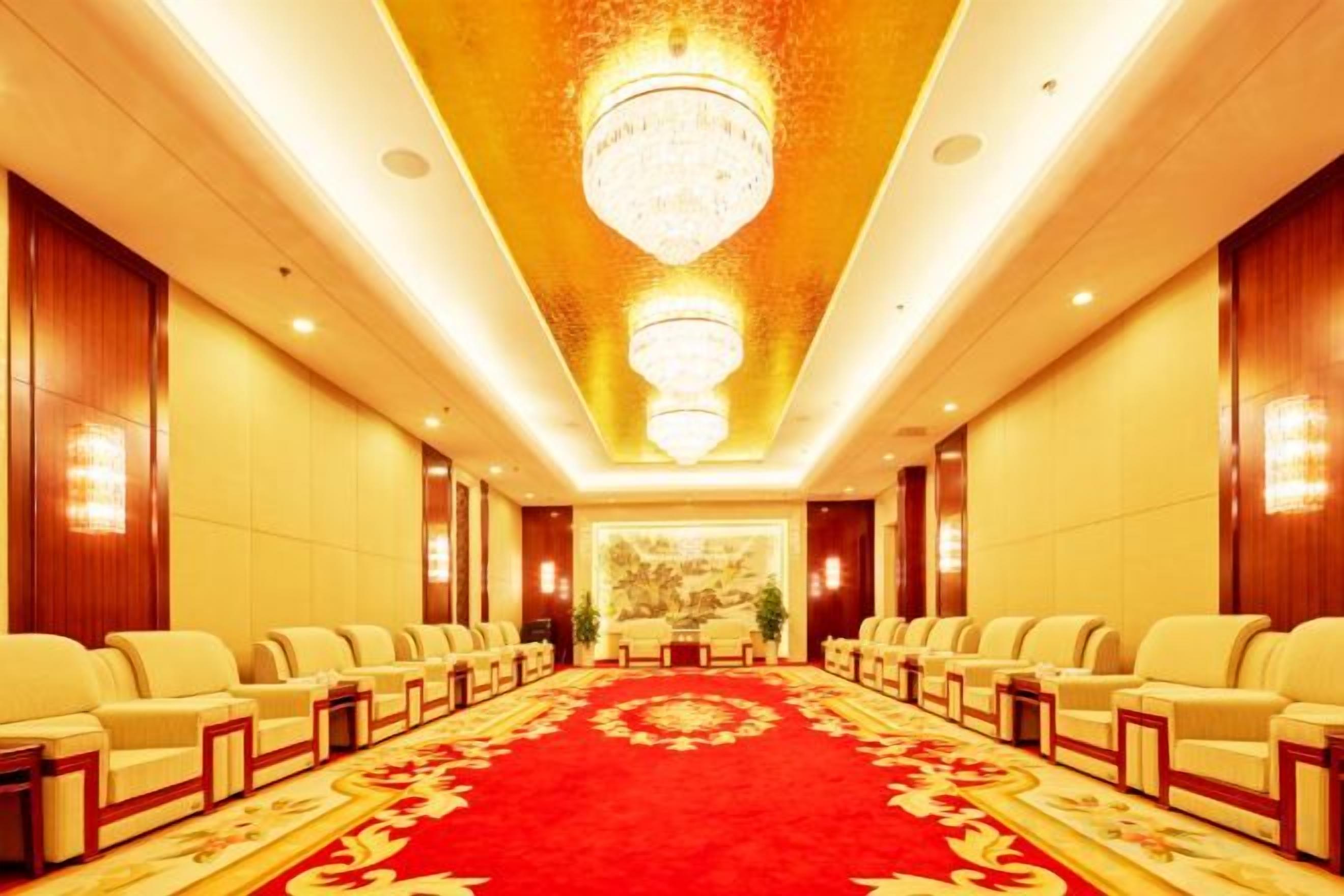 Un salón de conferencias de hotel con filas de sillas, alfombra roja y un candelabro.
