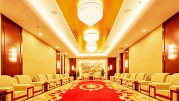 Un salón de conferencias de hotel con filas de sillas, alfombra roja y un candelabro.