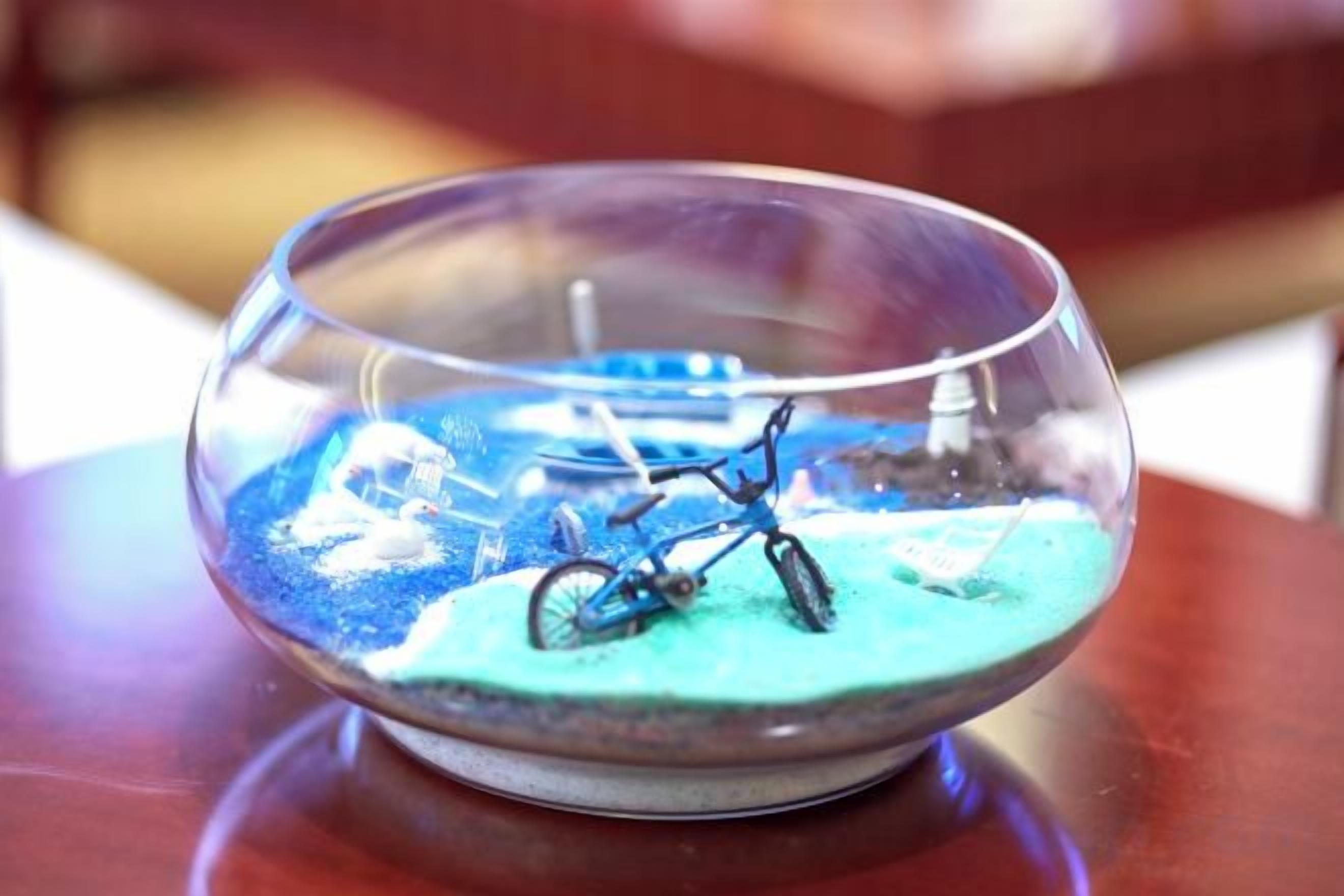 A clear glass bowl with a bicycle model inside, placed on a wooden surface.