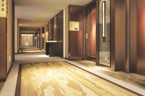A hotel corridor with wooden flooring, doors, and a trash bin. - Huaxi Hotel (Laixi)