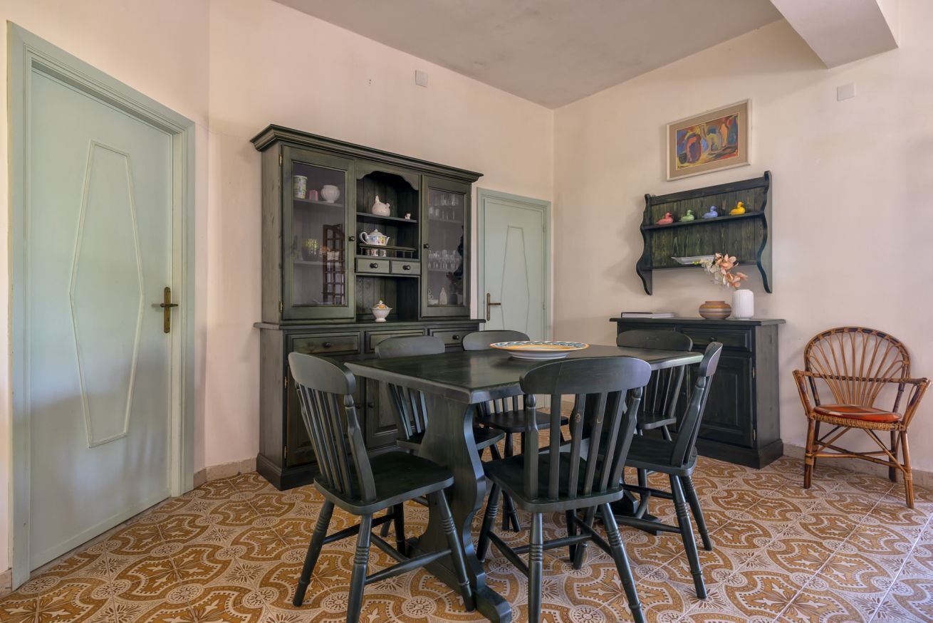 A dining area with a dark wooden table and chairs, a green cabinet with glass doors, and patterned floor tiles.