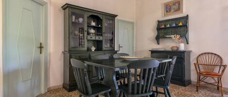 A dining area with a dark wooden table and chairs, a green cabinet with glass doors, and patterned floor tiles.
