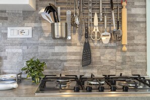 A kitchen with a gas stove, hanging utensils, and a potted plant.