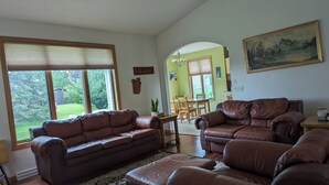 A spacious living room with leather sofas, a dining area with wooden furniture, and a view of a green landscape through large windows. -   LARGE HOME 30 mi TO LAMBEAU FIELD GREEN BAY AND ONLY 25 mi to EAA OSHKOSH (Appleton)