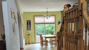 A spacious room with a wooden floor, a dining area with a table and chairs, a staircase with wooden railings, and a large window with blinds. -   LARGE HOME 30 mi TO LAMBEAU FIELD GREEN BAY AND ONLY 25 mi to EAA OSHKOSH (Appleton)