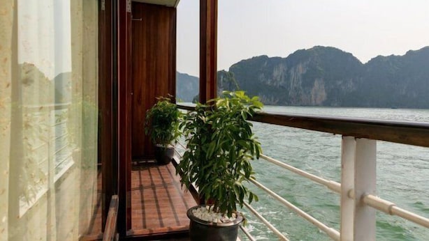 A balcony with potted plants, a wooden door, and a view of a mountainous coastline. - Pelican Classic Cruise (Tuan Chau)