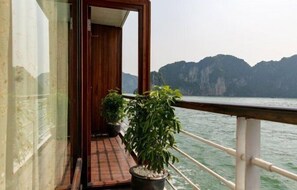A balcony with potted plants, a wooden door, and a view of a mountainous coastline. - Pelican Classic Cruise (Tuan Chau)