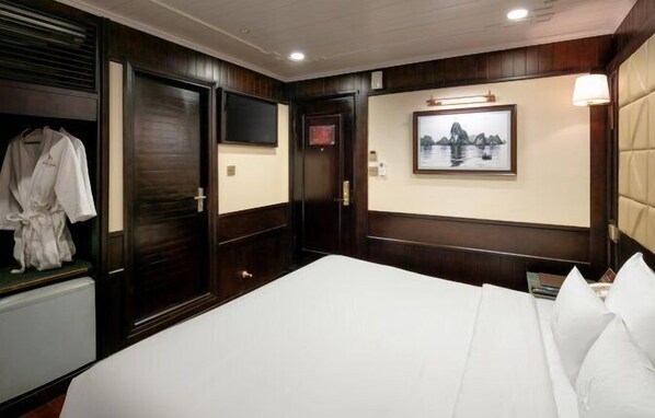 A hotel room with a large bed, wooden paneling, a robe hanging, a framed picture on the wall, and a door with a sign. - Pelican Classic Cruise (Tuan Chau)