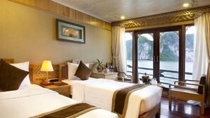 A hotel room with two beds, a wooden floor, a window with a view of the water, and a framed picture on the wall. - Pelican Classic Cruise (Tuan Chau)