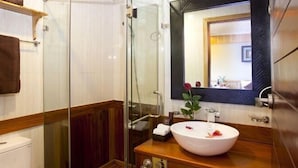 A bathroom with a glass shower enclosure, a wooden vanity with a white sink, and a mirror with a decorative frame. - Pelican Classic Cruise (Tuan Chau)